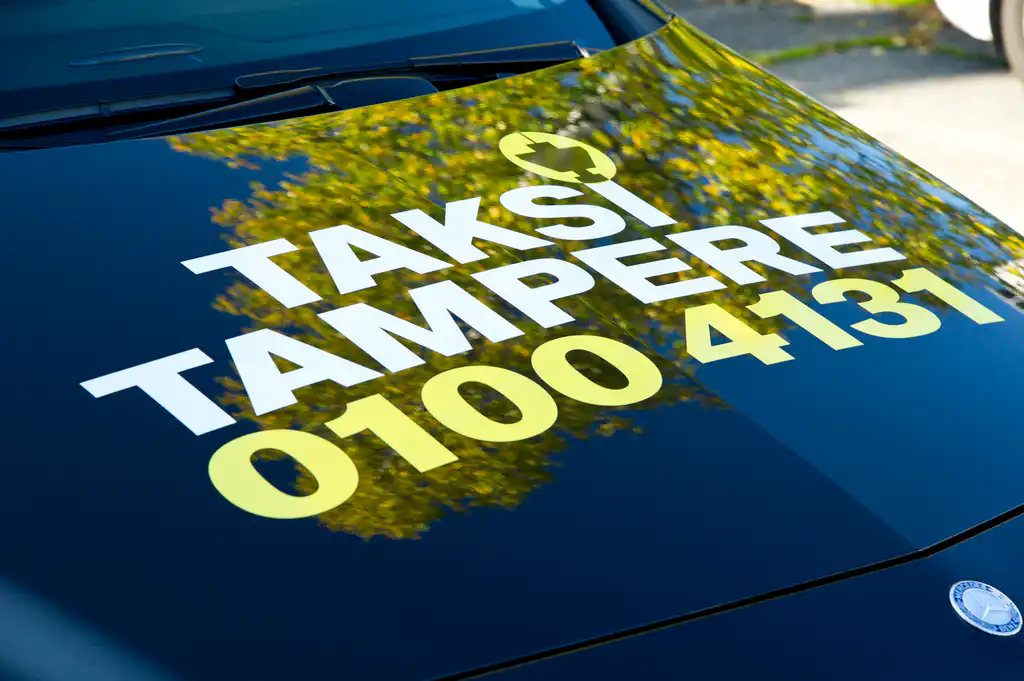 Kuvassa naisen käsi oven kahvassa ja valkoisella seinällä on Taksi Tampere -logo.