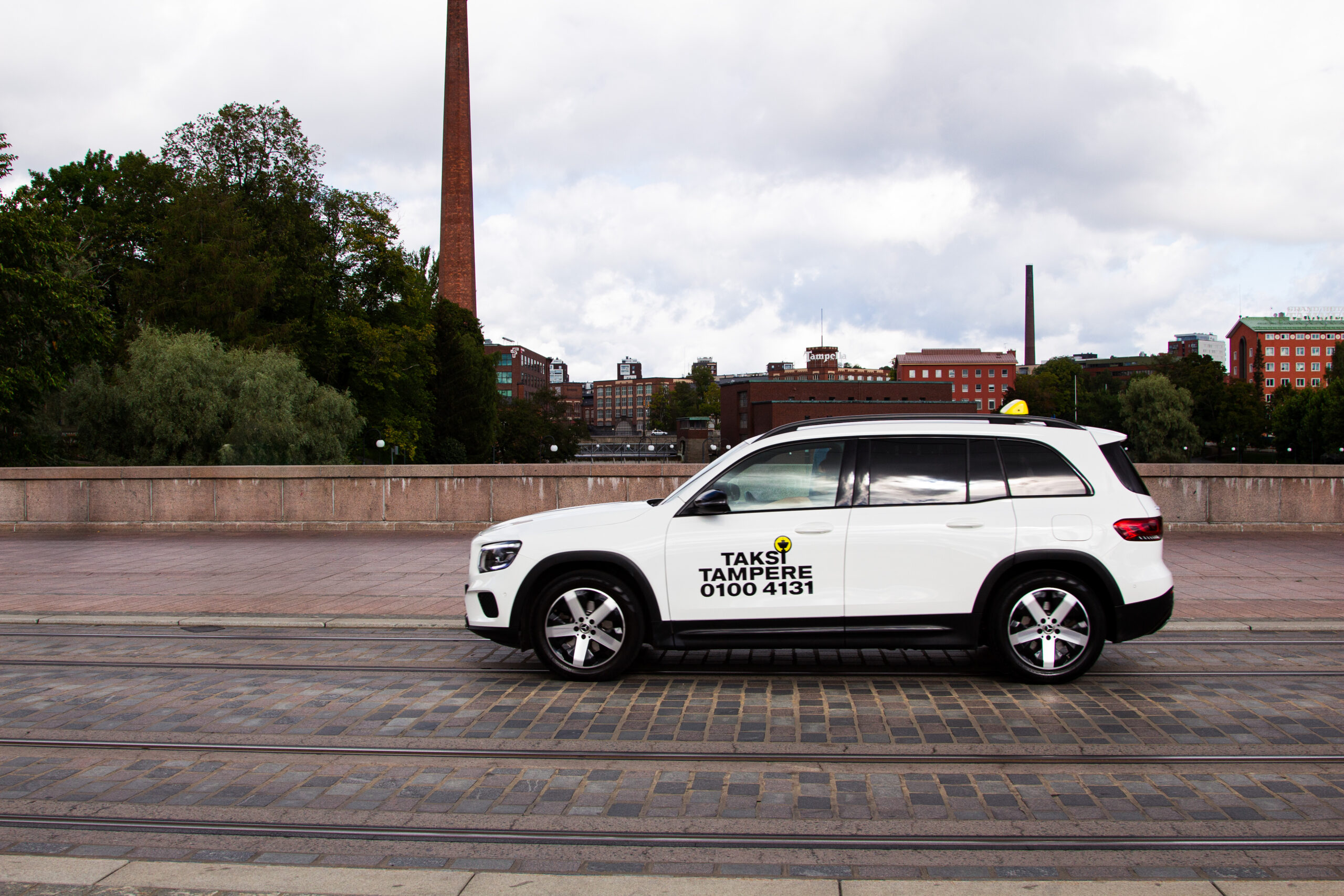 Kuvassa valkoinen Taksi Tampere logolla varusteltu taksiauto Hämeensillalla.
