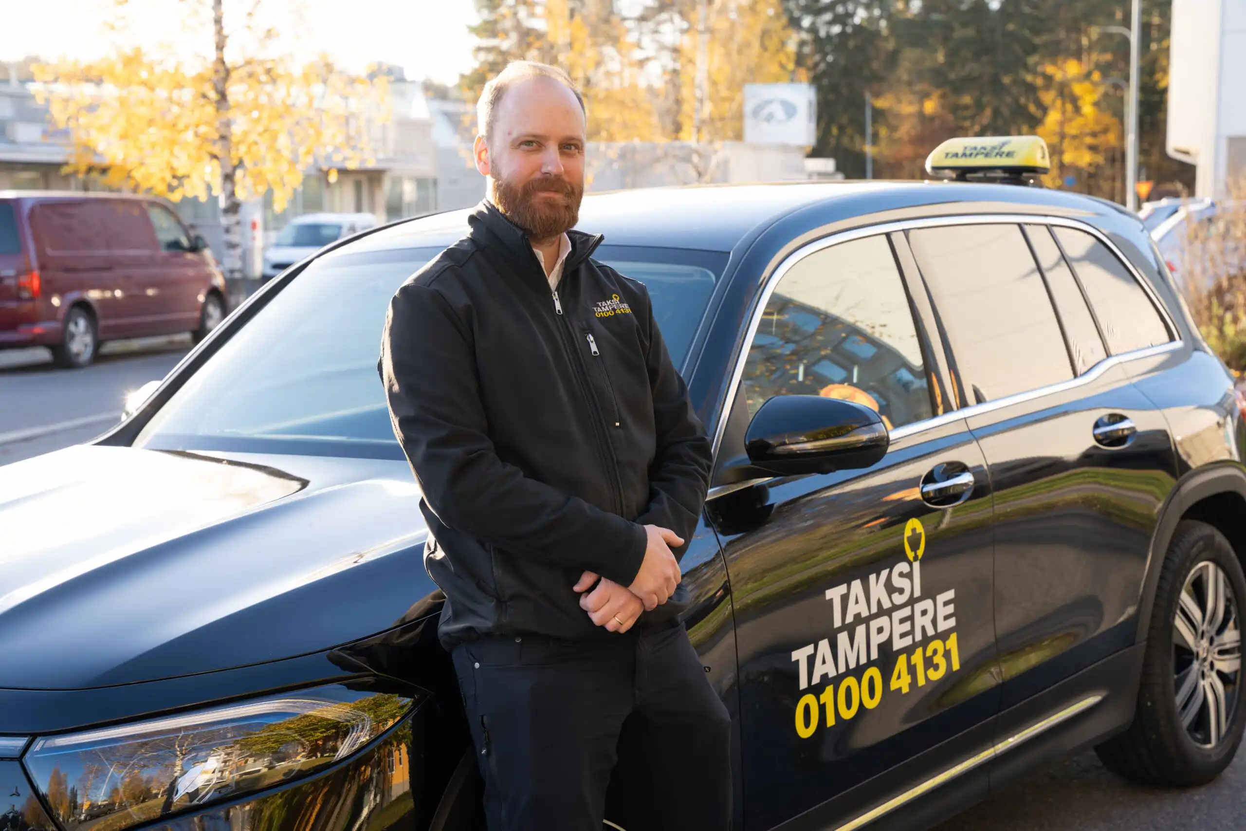 Miestaksinkuljettaja seisoo mustan Taksi Tampere logolla varustetun vieren auton sivussa ja katsoo kameraan.