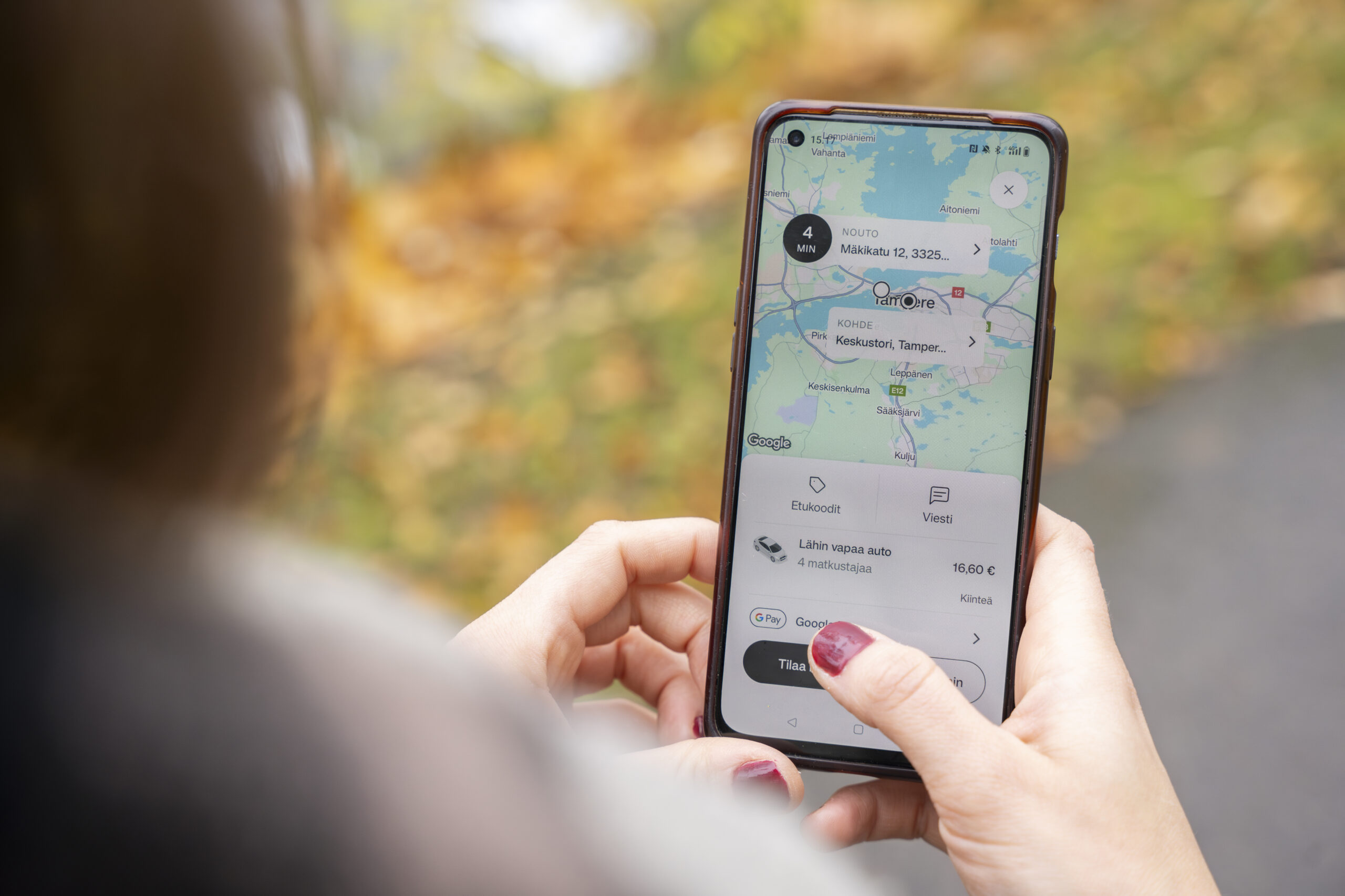 Kuvassa naisasiaks, jolla on kädessä puhelin, jonka näytöllä on Taksi Tampere -sovellus.